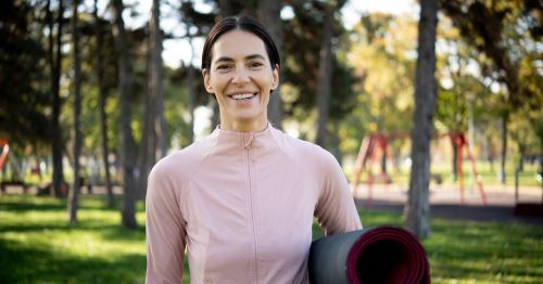 Mujer de 40 años en premenopausia sonriendo y sosteniendo una esterilla de yoga